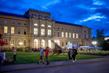 Naturkundemuseum bei Nacht von außen, viele Besucherinnen und Besucher davor